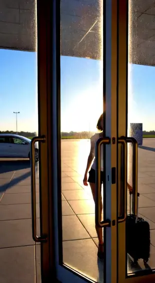 AI Video: Visual: Slow motion entry, foreign girl stepping out of airport, sunlight on...