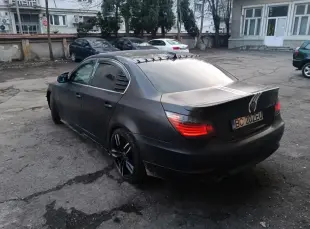AI Video: Matte black BMW 5 Series E60 with racing stripes and black sport rims driving...